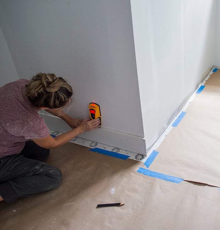 using a stud finder to find studs along the baseboard