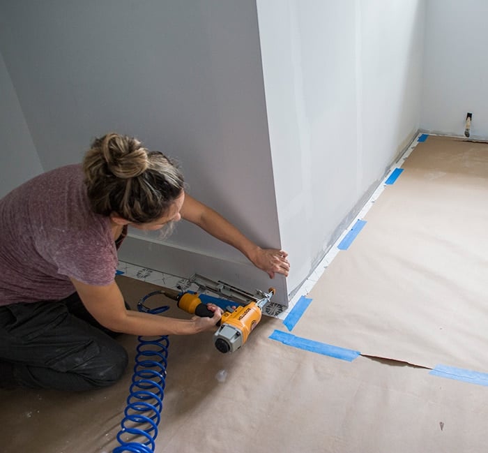 using a nailgun to attach 1x6 baseboards into a wall