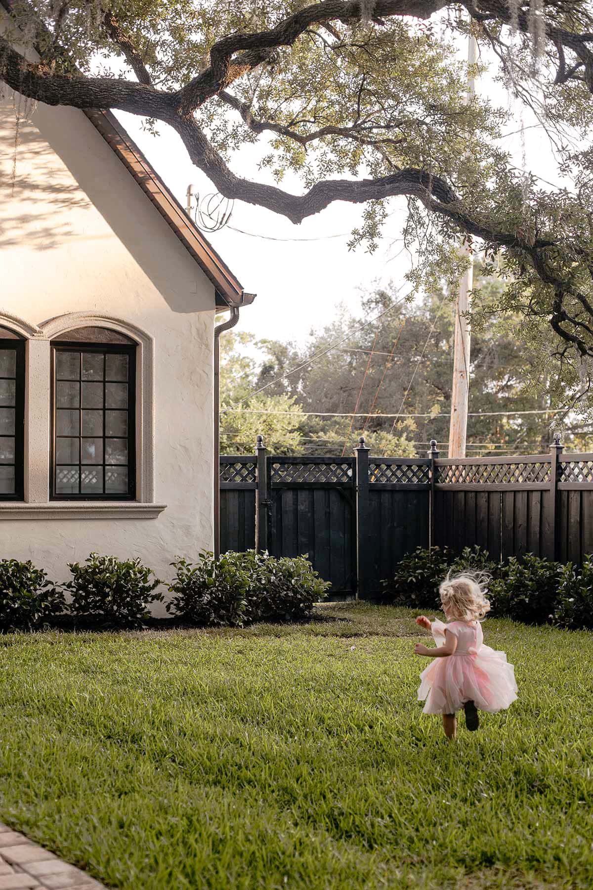 girl running on grass in backyard with black fence and house