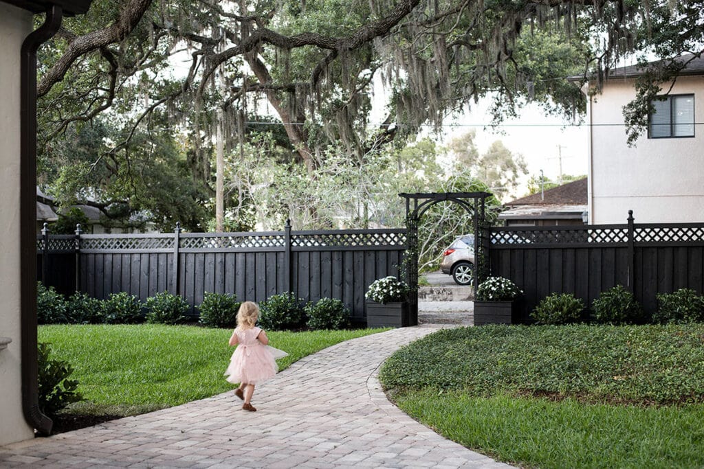 girl in backyard with black fence and greenery