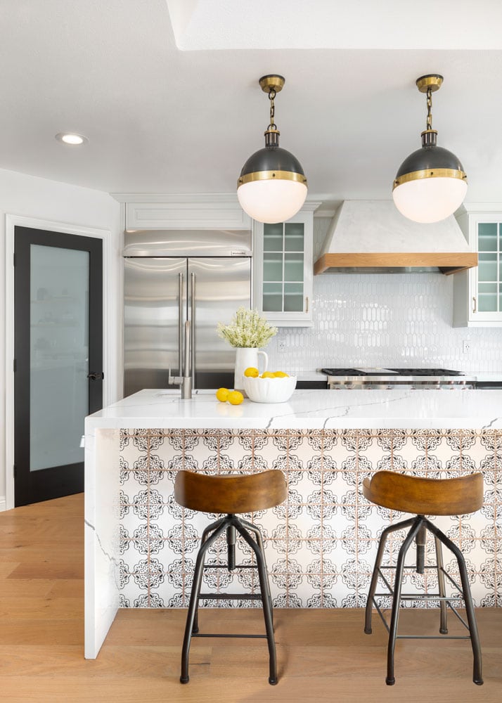 white kitchen with island with patterned tile, wood bar stools, wood floors