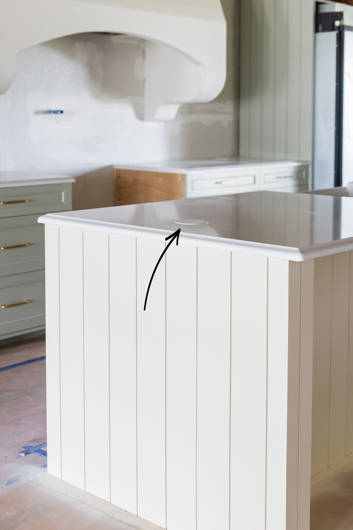 arrow pointing to a white countertop popup outlet in a kitchen island