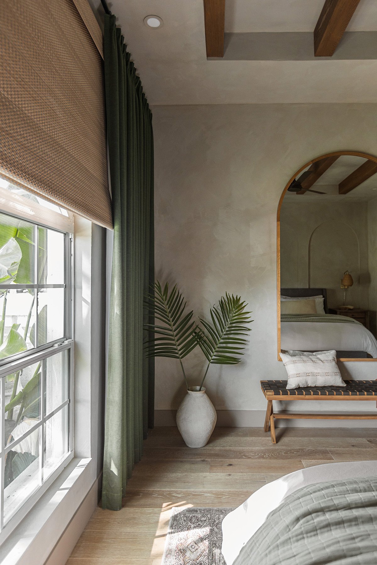 guest bedroom with lime wash walls, wood arched mirror and dark green curtains