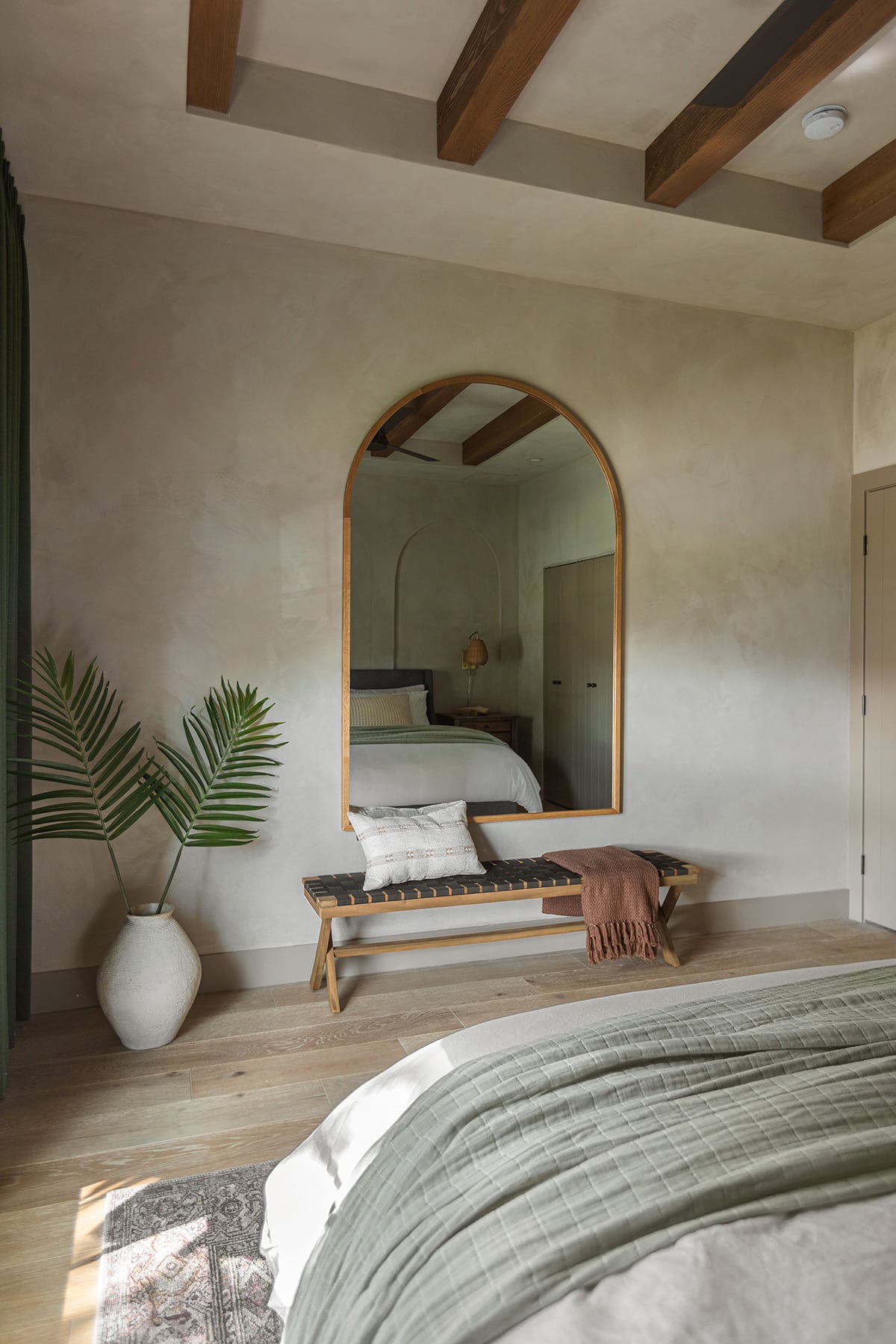 guest bedroom with lime wash walls, wood arched mirror and bench