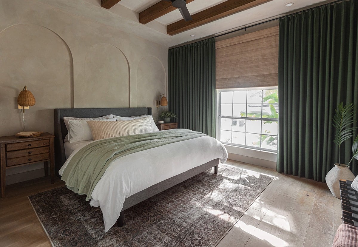 modern mediterranean style bedroom with dark green curtains, limewash walls, ceiling beams