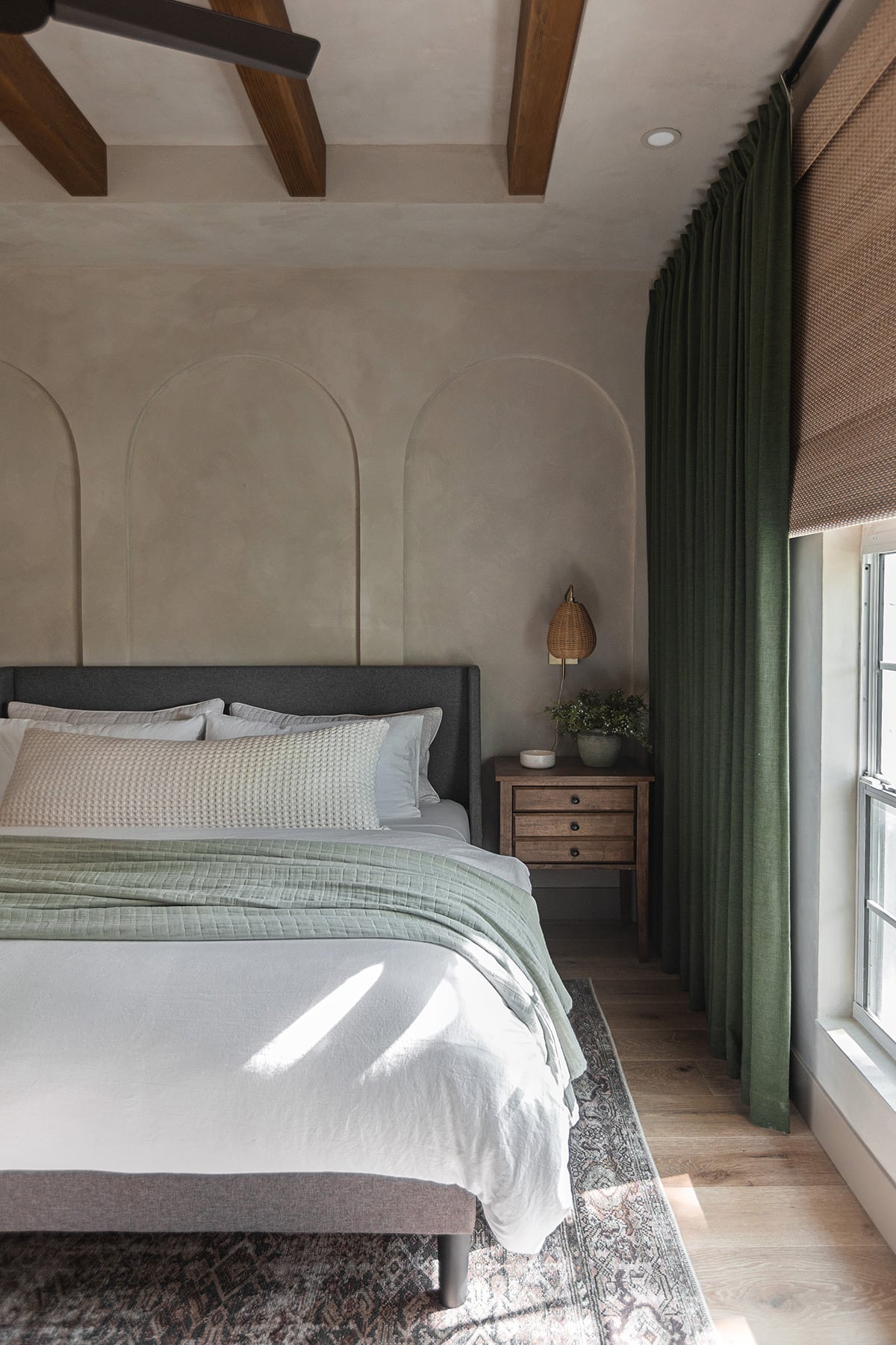 guest bedroom with lime wash walls, wood beams and dark green curtains