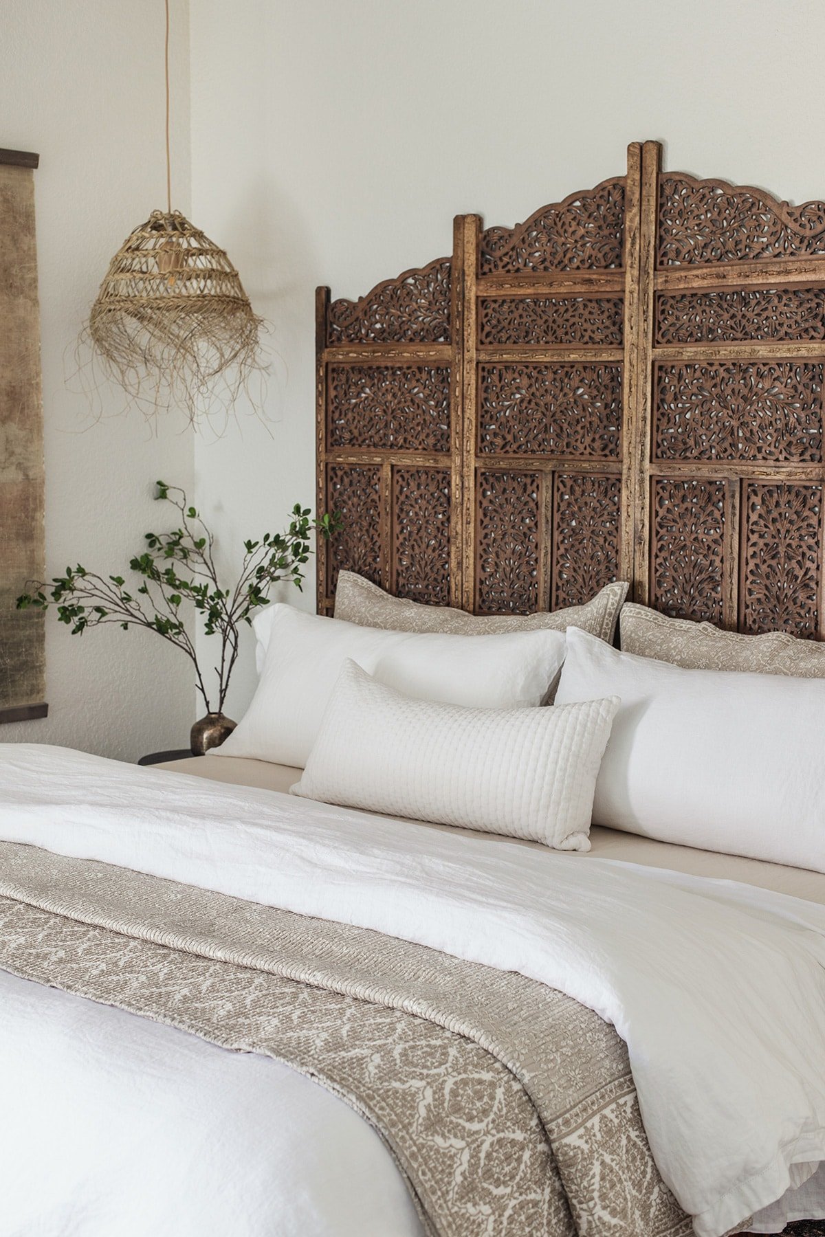 moroccan style bedroom with carved wood headboard and straw pendant lights, linen bedding
