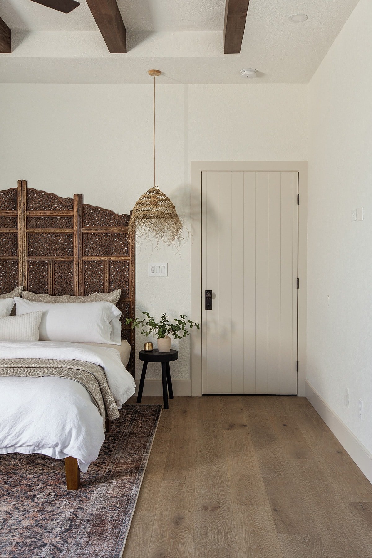 neutral bedroom with dark wood ceiling beams, carved wood headboard and alabaster paint