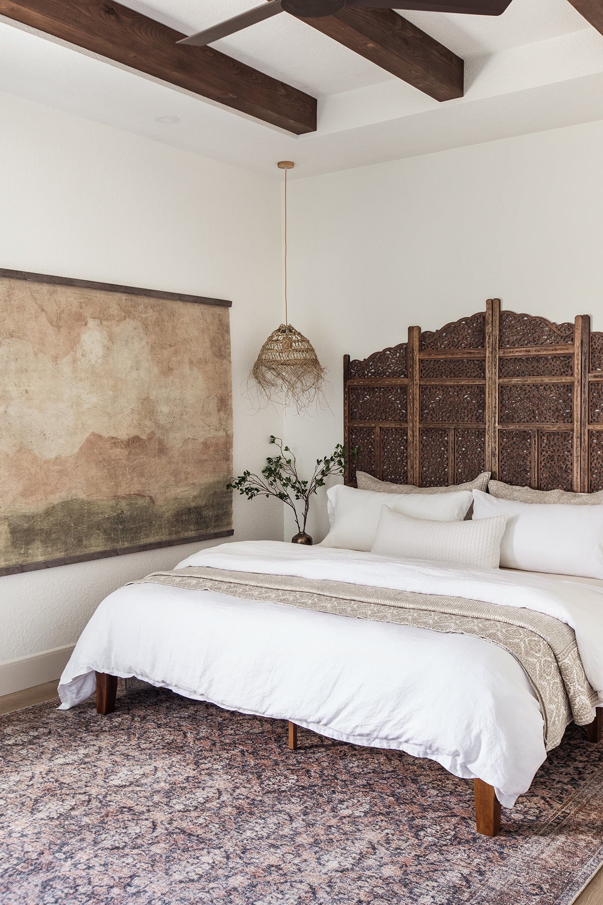 neutral bedroom with alabaster walls, tapestry and carved wood room divider headboard