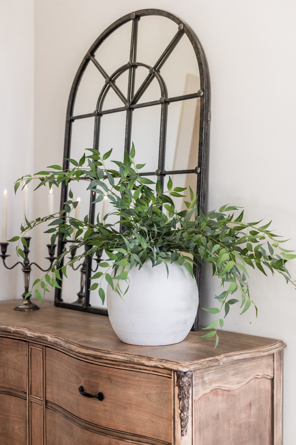 artificial italian ruscus branches in large white vase on dresser