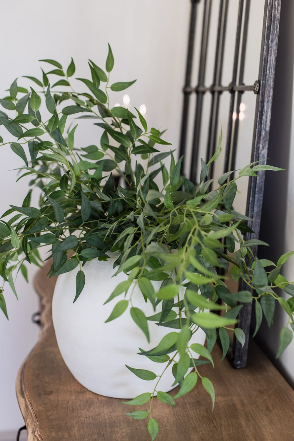 artificial italian ruscus branches in large white vase on dresser