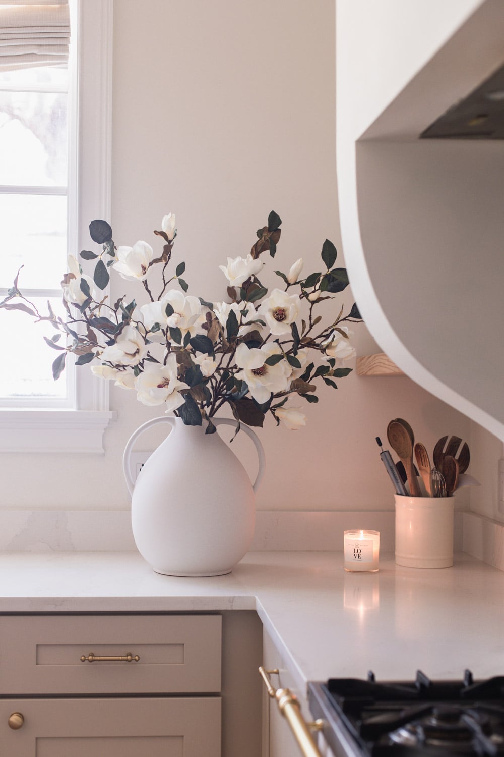 artificial magnolia flower branch in vase on kitchen counter