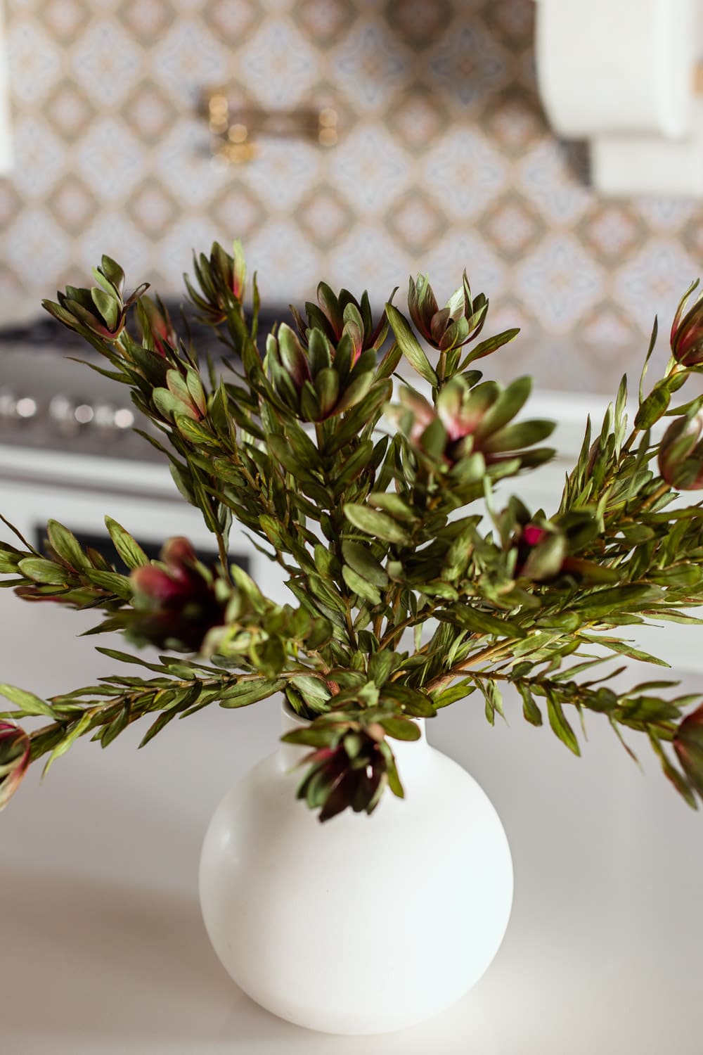 faux wild protega stems in vase on kitchen island