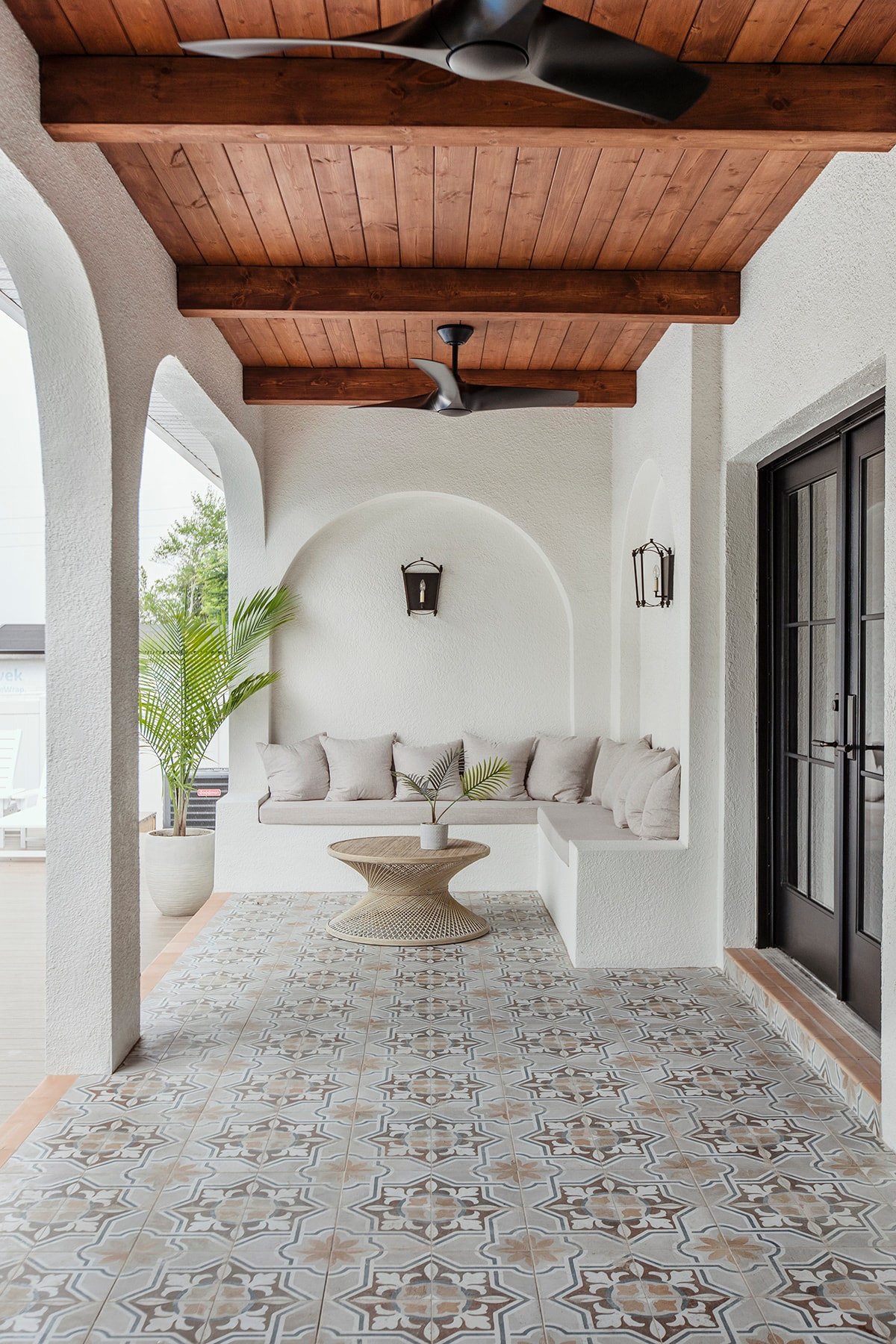spanish style porch with wood beam ceiling, patterned tile and black french doors, and arches