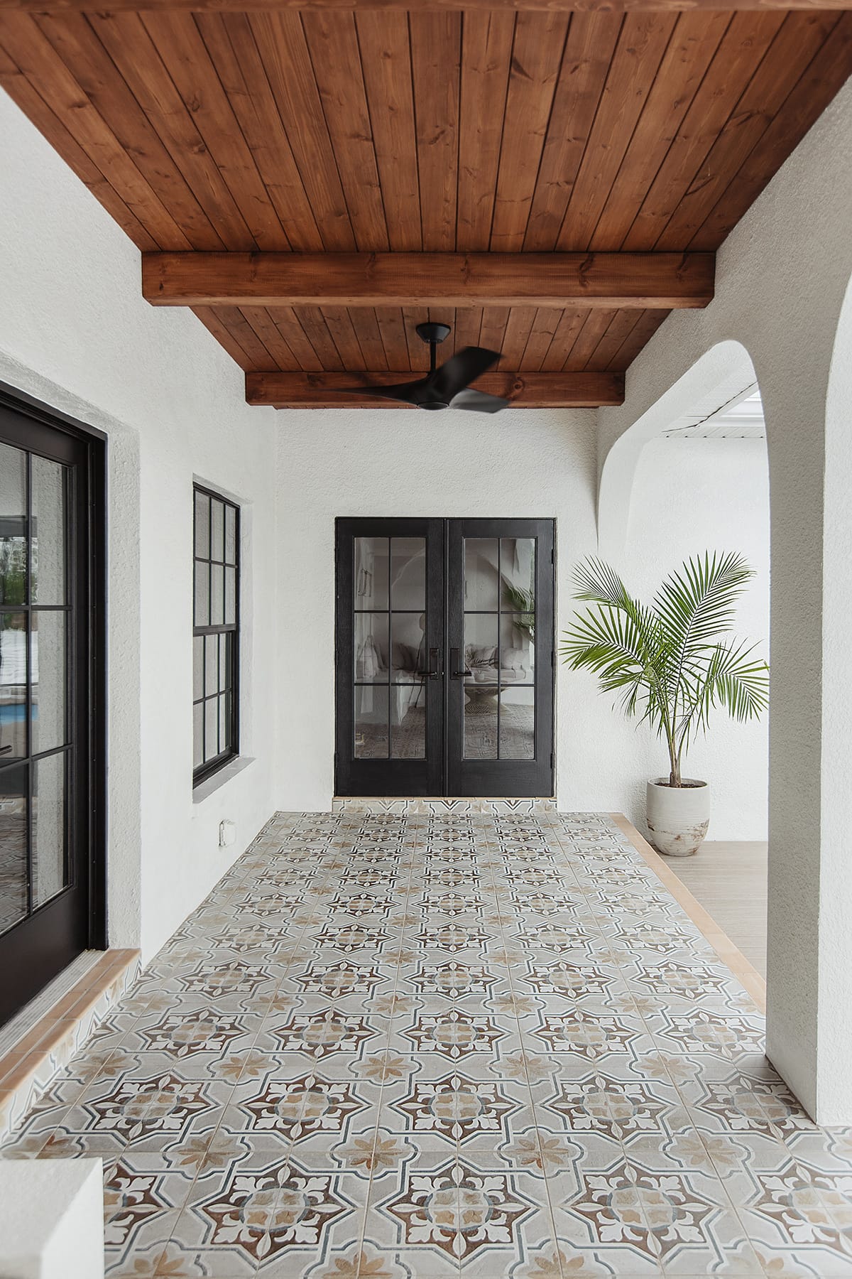 mediterranean porch with wood beam ceiling, patterned tile and black french doors