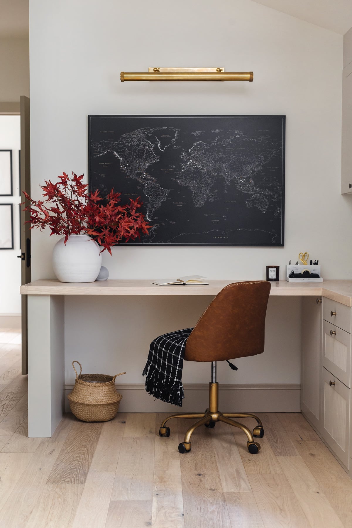 office with large black world map, picture light, desk and leather chair