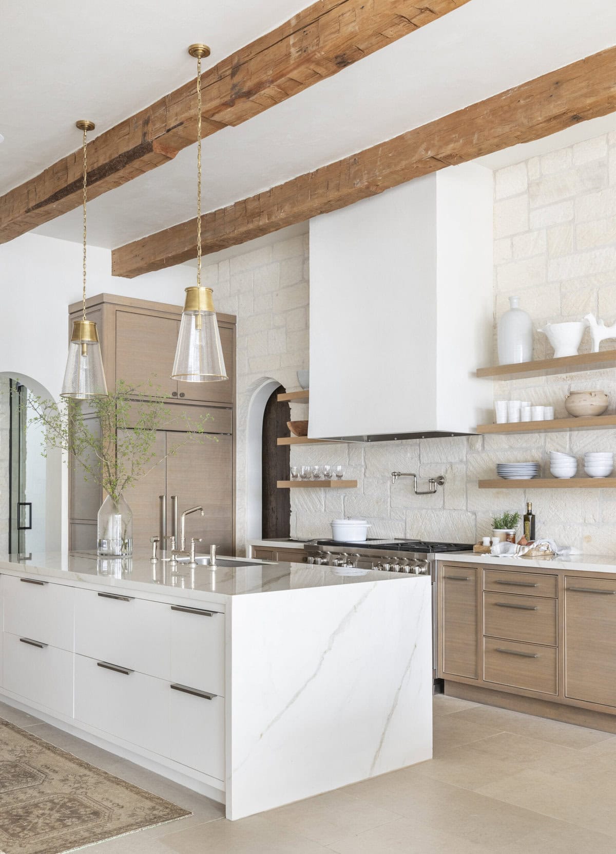 white and wood kitchen with ceiling beams and stone wall