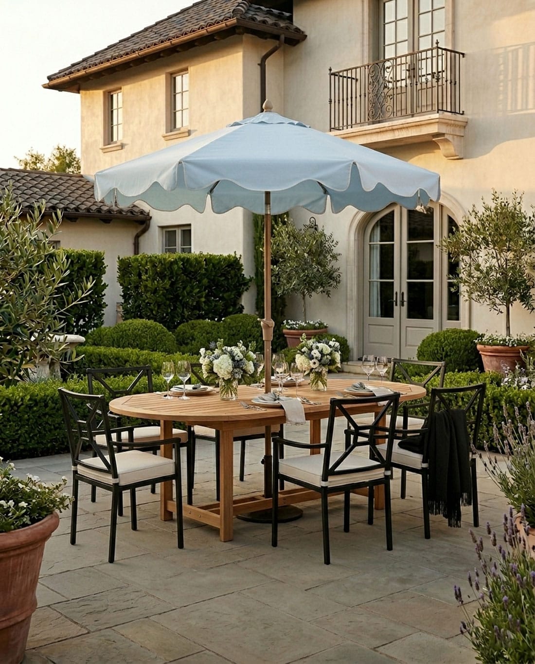 blue scalloped patio umbrella with a teak dining table and black metal chairs